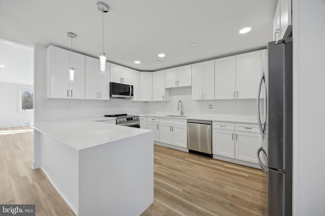 kitchen with sink, hanging light fixtures, stainless steel appliances, light hardwood / wood-style flooring, and white cabinets