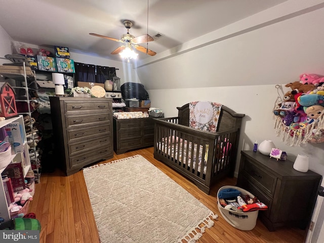 bedroom featuring ceiling fan, vaulted ceiling, a nursery area, and light wood-type flooring