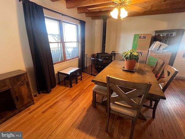 dining room featuring ceiling fan, a wood stove, beam ceiling, and light wood-type flooring