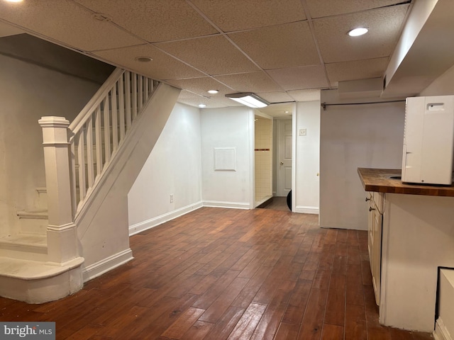 basement with a drop ceiling and dark wood-type flooring