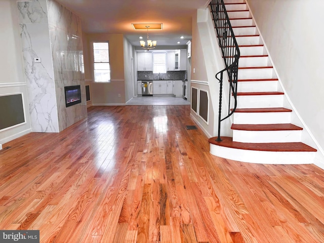 unfurnished living room featuring a chandelier, light wood-type flooring, sink, and a tiled fireplace