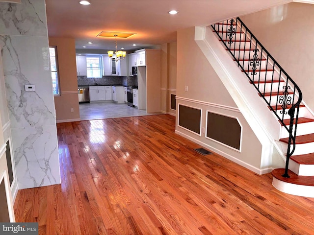 unfurnished living room with light hardwood / wood-style flooring, a notable chandelier, and sink