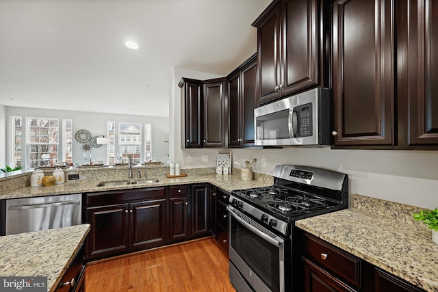 kitchen featuring light stone countertops, stainless steel appliances, light hardwood / wood-style floors, and sink