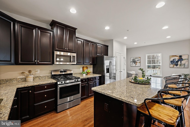 kitchen with light stone counters, light hardwood / wood-style flooring, a kitchen bar, a kitchen island, and appliances with stainless steel finishes