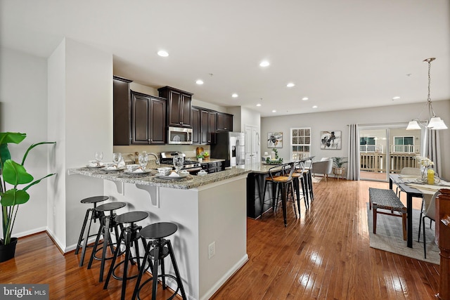 kitchen featuring a breakfast bar, appliances with stainless steel finishes, decorative light fixtures, light stone counters, and kitchen peninsula