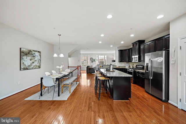 kitchen with light stone countertops, a center island, stainless steel appliances, decorative light fixtures, and a breakfast bar