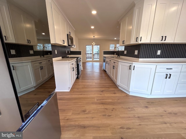 kitchen with appliances with stainless steel finishes, sink, decorative light fixtures, light hardwood / wood-style flooring, and white cabinetry