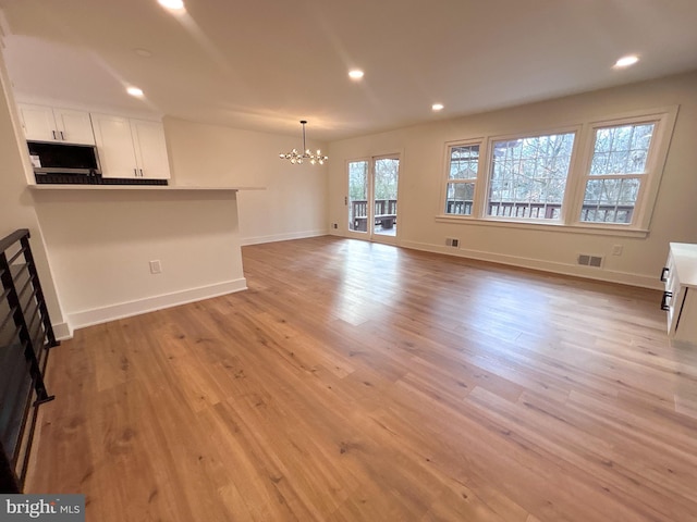 unfurnished living room with an inviting chandelier and light wood-type flooring