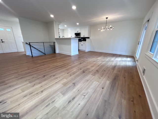 unfurnished living room featuring light wood-type flooring and a notable chandelier