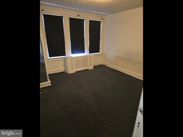 unfurnished room featuring radiator, a textured ceiling, and dark colored carpet