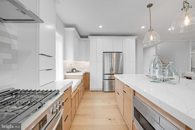 kitchen featuring light stone counters, decorative light fixtures, light wood finished floors, tasteful backsplash, and appliances with stainless steel finishes