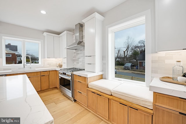 kitchen with light stone counters, light wood finished floors, stainless steel gas stove, a sink, and wall chimney range hood