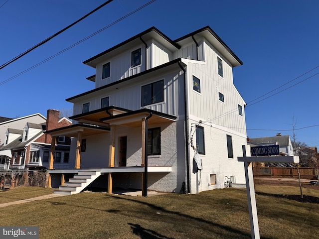 view of front of home featuring brick siding, covered porch, board and batten siding, a front yard, and stairs