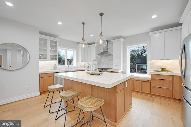 kitchen with stainless steel appliances, a breakfast bar, a kitchen island, light wood-style floors, and wall chimney range hood