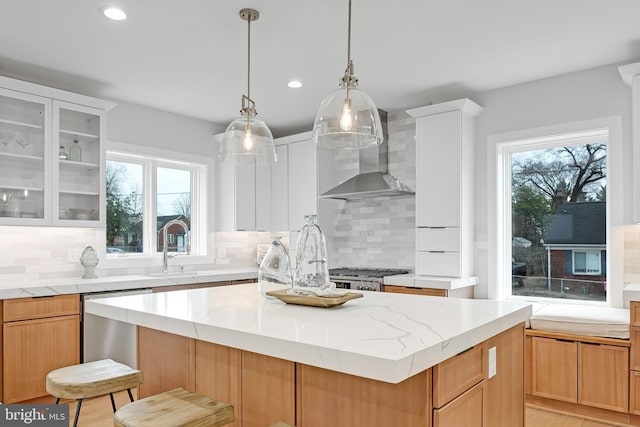 kitchen featuring a center island, glass insert cabinets, a sink, wall chimney range hood, and range