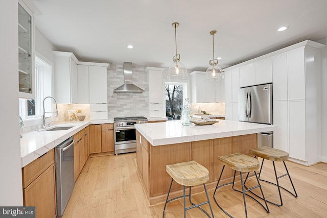 kitchen with light wood-style floors, a center island, stainless steel appliances, wall chimney range hood, and a sink