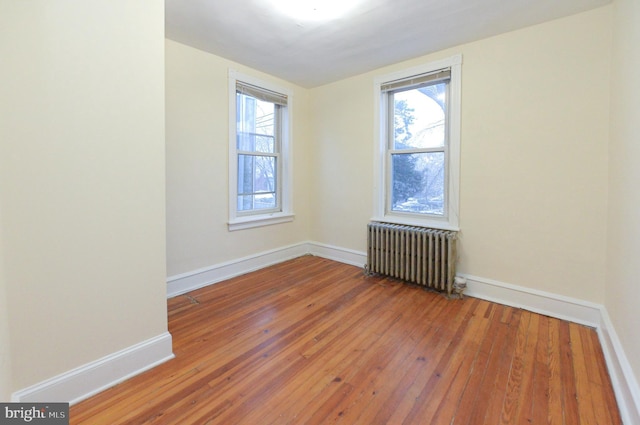 empty room featuring a healthy amount of sunlight, radiator heating unit, and hardwood / wood-style floors