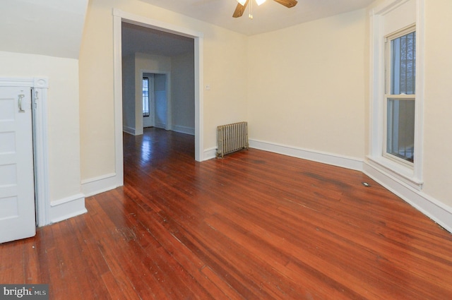 empty room featuring dark hardwood / wood-style floors, radiator, and ceiling fan