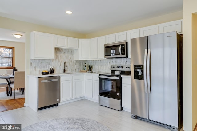 kitchen with sink, backsplash, white cabinets, and appliances with stainless steel finishes