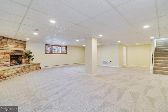 basement with a stone fireplace, a baseboard heating unit, a paneled ceiling, and light colored carpet