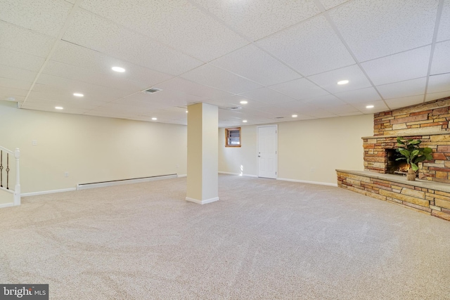 basement with baseboard heating, a paneled ceiling, a stone fireplace, and carpet floors