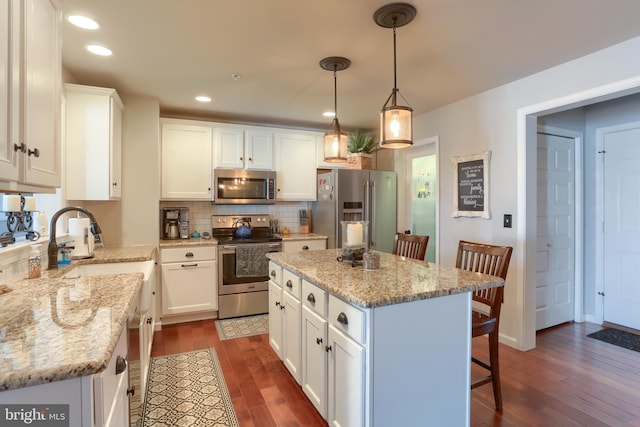 kitchen featuring appliances with stainless steel finishes, light stone counters, pendant lighting, a center island, and white cabinetry