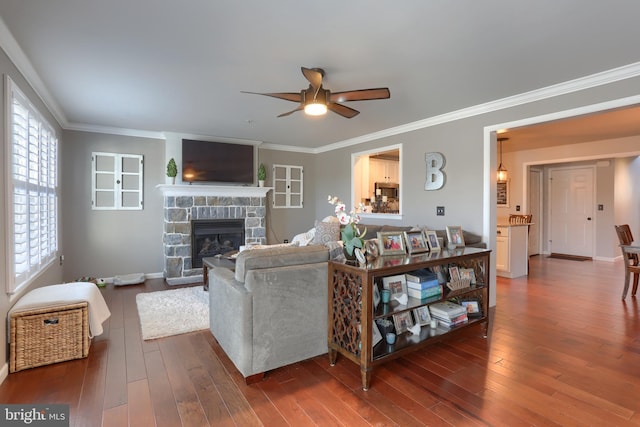 living room with a stone fireplace, ceiling fan, crown molding, and dark hardwood / wood-style floors