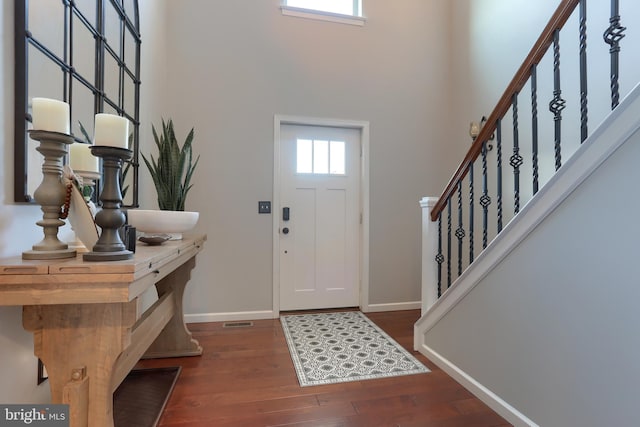 foyer with a towering ceiling, dark wood-type flooring, and a healthy amount of sunlight