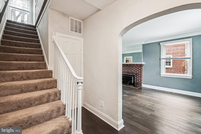 stairs featuring ornamental molding, hardwood / wood-style floors, and a brick fireplace