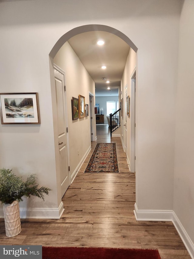 hall featuring baseboards, arched walkways, wood finished floors, and recessed lighting