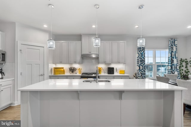 kitchen with sink, hanging light fixtures, backsplash, and an island with sink