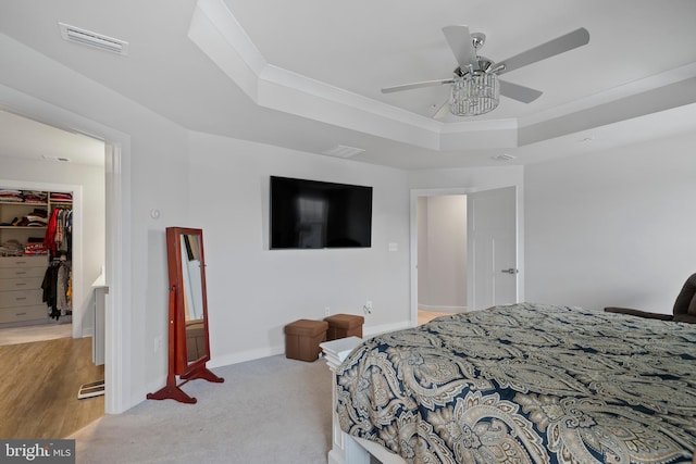 carpeted bedroom with ceiling fan, a raised ceiling, crown molding, a spacious closet, and a closet