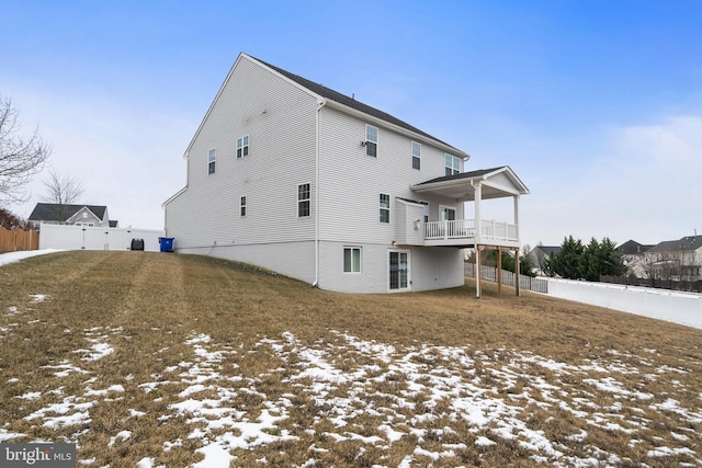 snow covered back of property featuring a balcony and a yard