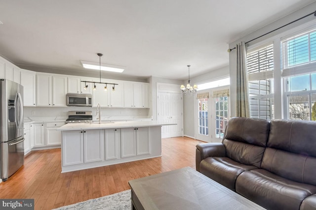 kitchen with decorative light fixtures, white cabinetry, an island with sink, stainless steel appliances, and light hardwood / wood-style flooring