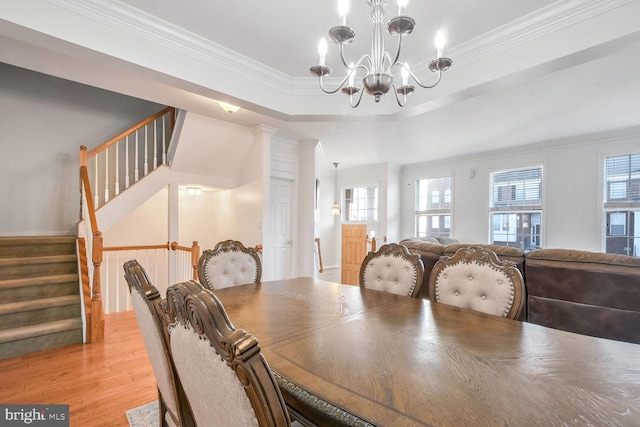 dining space featuring crown molding, a tray ceiling, a chandelier, and light wood-type flooring