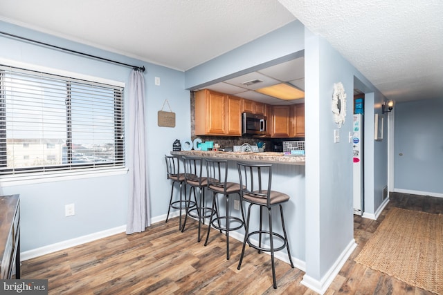 kitchen with tasteful backsplash, a kitchen breakfast bar, kitchen peninsula, dark wood-type flooring, and a textured ceiling