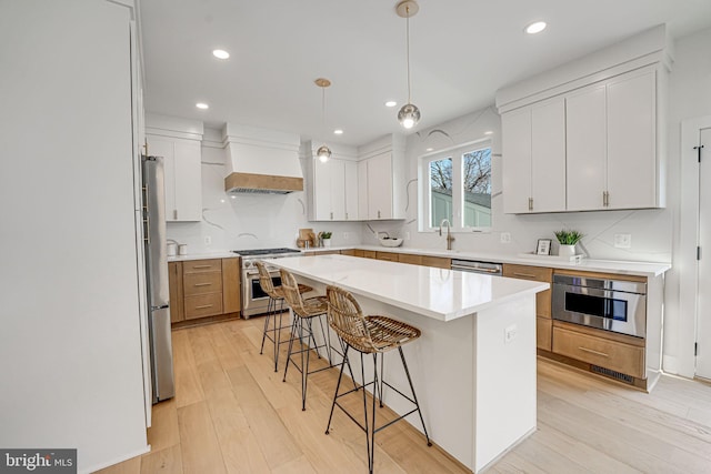 kitchen featuring custom exhaust hood, white cabinetry, decorative light fixtures, appliances with stainless steel finishes, and a kitchen island