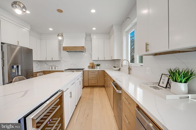 kitchen featuring premium range hood, appliances with stainless steel finishes, white cabinetry, hanging light fixtures, and light stone countertops