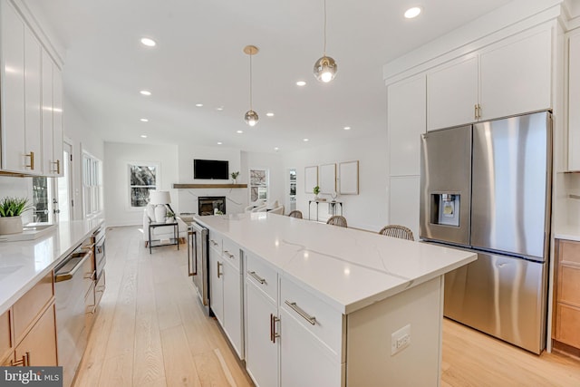 kitchen featuring white cabinetry, hanging light fixtures, a center island, stainless steel appliances, and light stone countertops