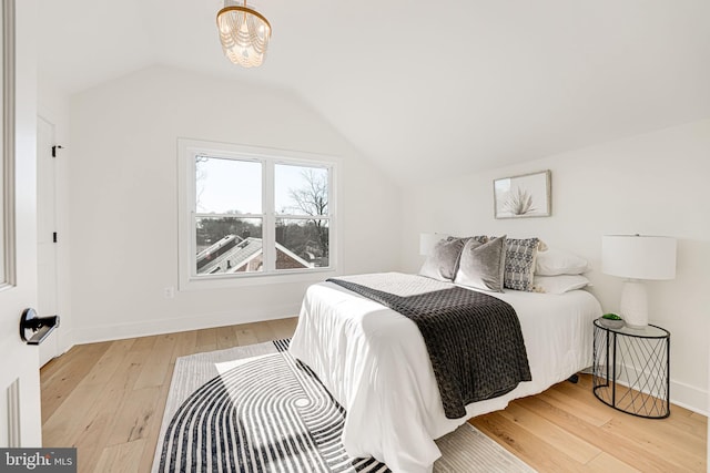 bedroom featuring vaulted ceiling, a notable chandelier, and light hardwood / wood-style flooring