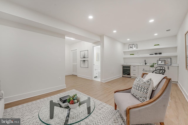 living area featuring light hardwood / wood-style flooring, beverage cooler, and indoor wet bar