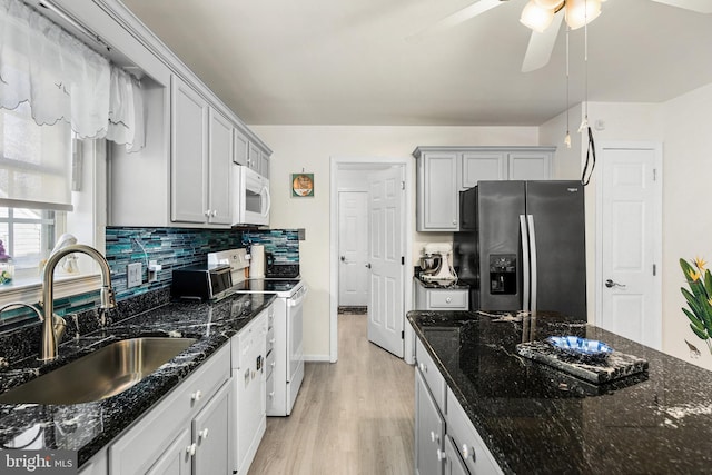 kitchen with white appliances, backsplash, dark stone counters, sink, and ceiling fan