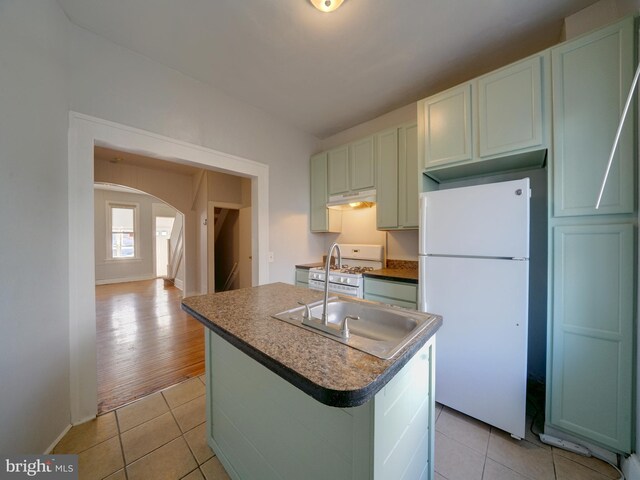 kitchen featuring light tile patterned floors, an island with sink, and white appliances