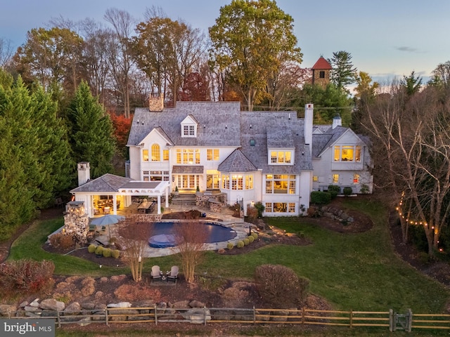 back house at dusk with a fenced in pool, a balcony, and a lawn