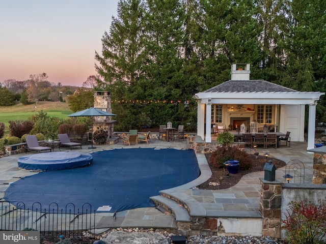 pool at dusk featuring a patio area and an outdoor fireplace