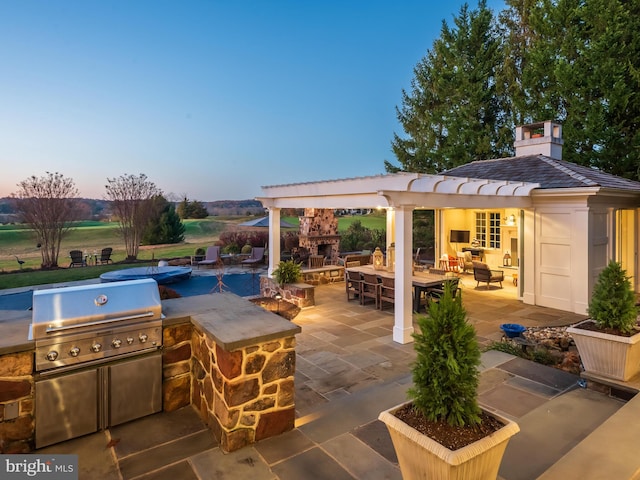 patio terrace at dusk featuring an outdoor living space with a fireplace and an outdoor kitchen