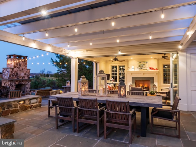 patio terrace at dusk with ceiling fan and an outdoor stone fireplace