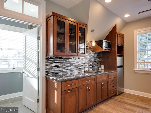 kitchen with decorative backsplash, dark stone counters, stainless steel appliances, light hardwood / wood-style floors, and lofted ceiling