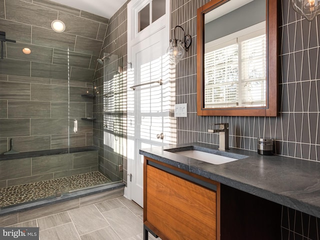 bathroom featuring tile patterned flooring, decorative backsplash, vanity, a shower with shower door, and tile walls