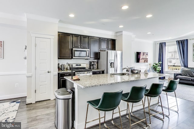 kitchen with an island with sink, appliances with stainless steel finishes, ornamental molding, and a breakfast bar area